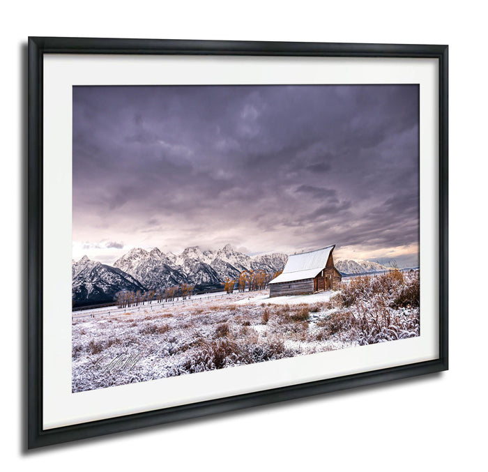 A snowy mountain landscape with a wooden barn in the foreground, set against a dramatic cloudy sky.
