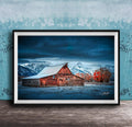 A rustic wooden barn stands in a snowy landscape, with a mountain range in the background under a dark, cloudy sky.