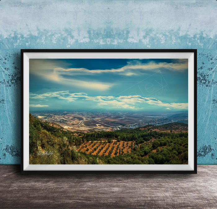 The image is a framed photograph of a scenic landscape, featuring a valley with a city in the distance, surrounded by mountains and trees.