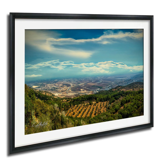 The image is a framed photograph of a scenic landscape, featuring a valley with a city in the distance, surrounded by mountains and trees.
