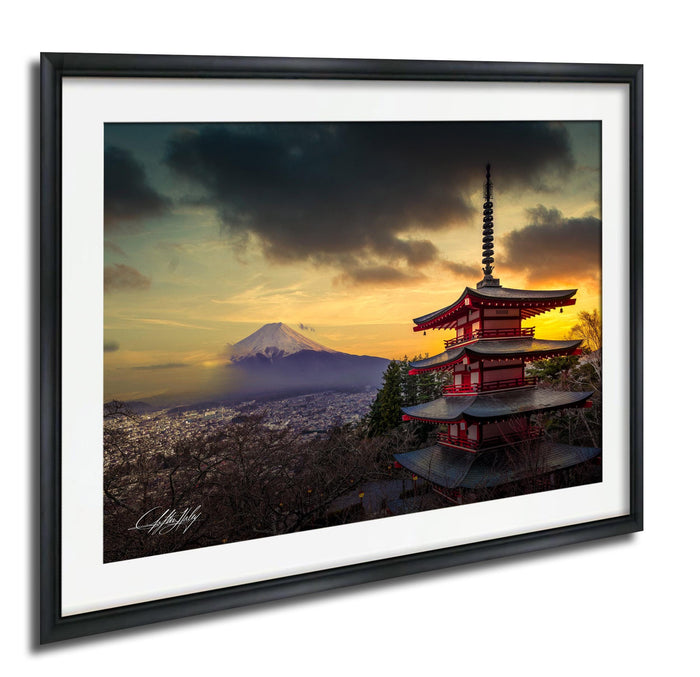 A framed photograph depicting a red pagoda with a mountain in the background, set against a dramatic sky with clouds and a sunset.