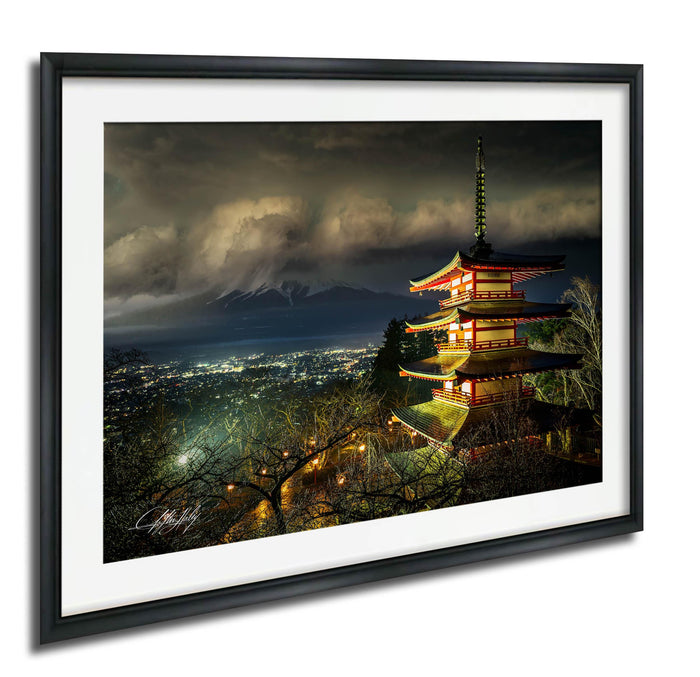 A framed photograph depicting a traditional Japanese pagoda illuminated at night, with a mountainous landscape in the background.