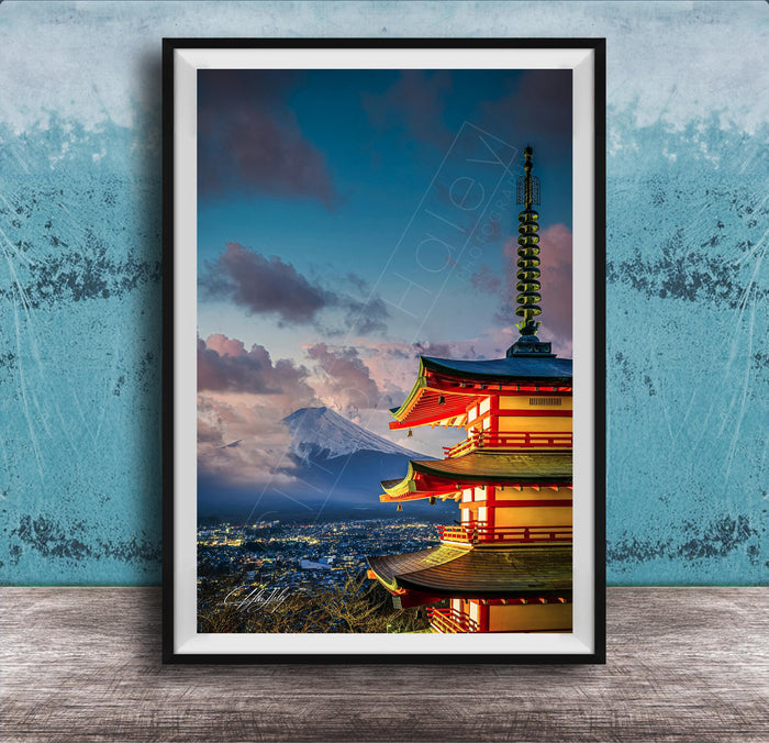 A framed photograph of a traditional Japanese pagoda, with a mountain range visible in the background, set against a blue sky with clouds.