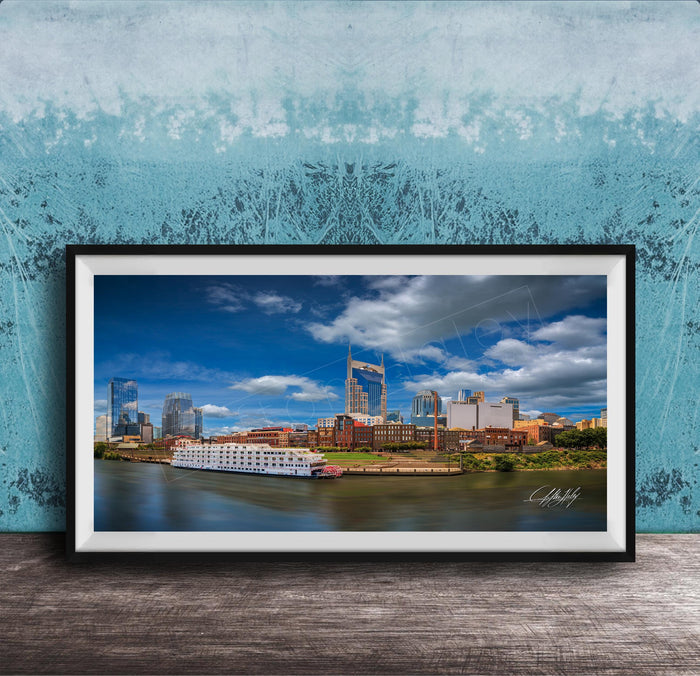 A framed photograph of a city skyline with a river in the foreground, featuring a large white boat on the water.