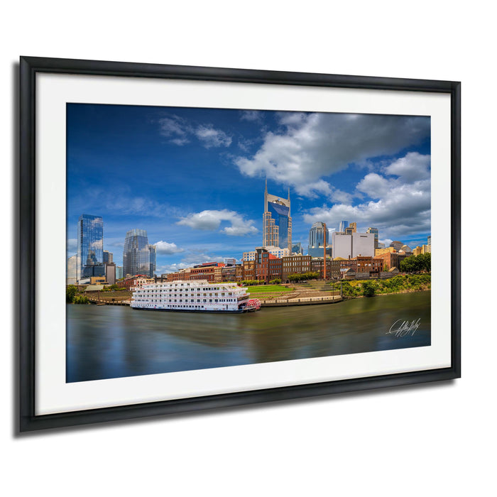 A framed photograph depicting the skyline of Nashville, Tennessee, with the city's iconic skyscrapers and a river running through the center.