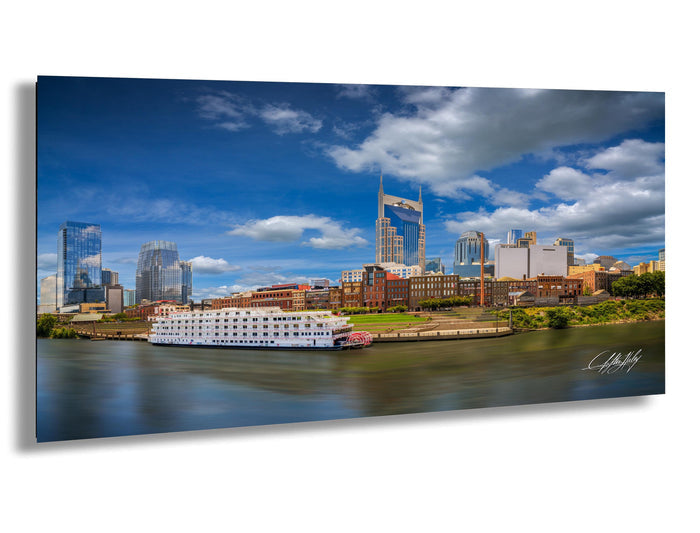 A large white boat is docked in a river, with the city skyline of Nashville, Tennessee, visible in the background.