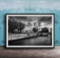 A black and white photograph of the Notre-Dame Cathedral in Paris, France, with a river and trees in the foreground.