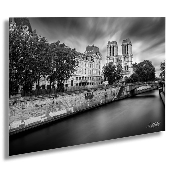 a serene cityscape with a river running through it, flanked by historic buildings and trees. The sky is filled with clouds, creating a dramatic backdrop for the scene.