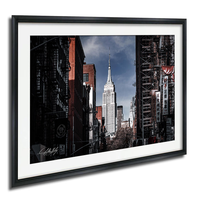 A framed photograph of the iconic Empire State Building in New York City, with the surrounding cityscape visible in the background.