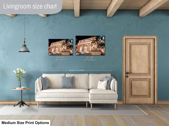 a living room with a white sofa, a wooden door, and a hanging light fixture. There are two framed photographs hanging on the wall, one depicting a building and the other showing a tree. The wall is painted a light blue color, and the floor is covered with a gray rug.