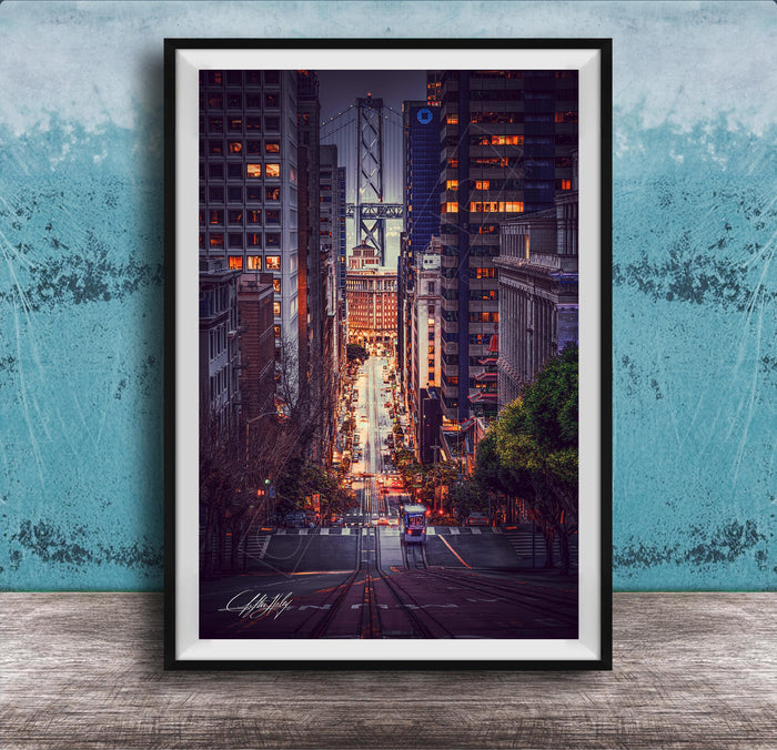 A framed photograph depicting a city street at night, with tall buildings and a bridge in the background. The street is illuminated by streetlights and the glow of the buildings, creating a vibrant and dynamic scene.