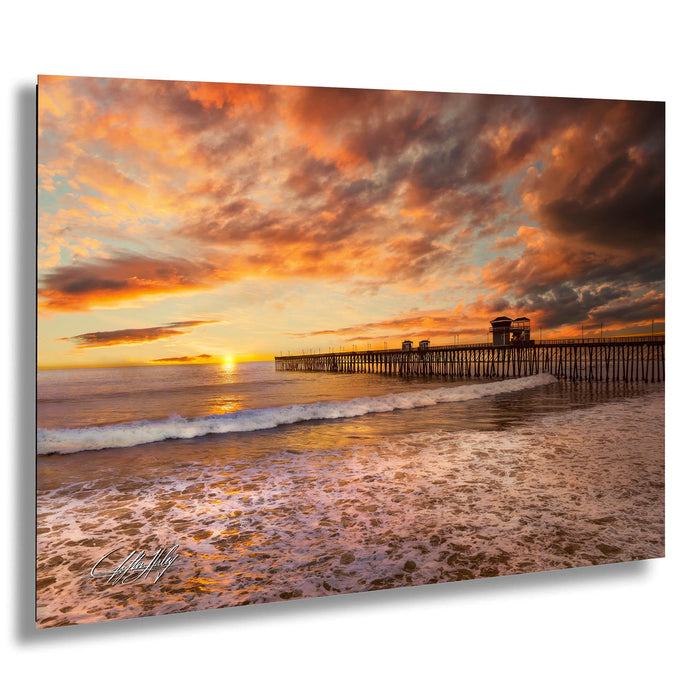 a serene beach scene at sunset, with a wooden pier extending into the calm waters. The sky is filled with vibrant orange and pink hues, creating a stunning backdrop for the tranquil setting.