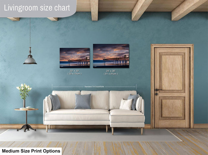 a living room with a white sofa, a wooden door, and a painting of a pier on the wall. The painting is of a sunset over the ocean, and the size of the painting is 24 inches by 36 inches.