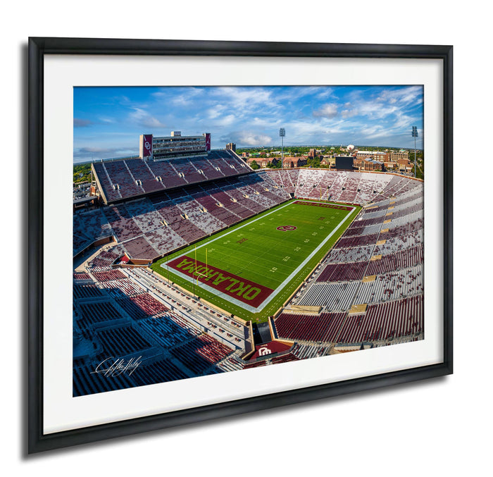 The image is a framed photograph of a football stadium with a large field, surrounded by rows of seating and a scoreboard.