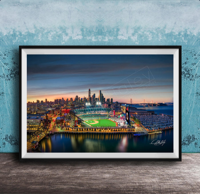 A framed aerial view of a city skyline at night, with a brightly lit stadium and surrounding buildings.
