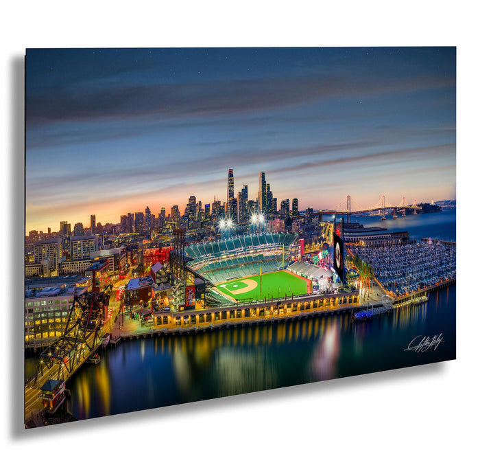 A vibrant nighttime view of a baseball stadium, with the city skyline and bridges in the background illuminated by colorful lights.