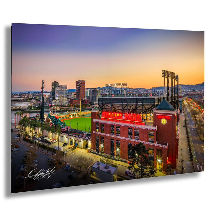 A vibrant cityscape at sunset, with a large stadium and surrounding buildings illuminated against a colorful sky.