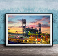 A framed photograph of a baseball stadium at sunset, with the stadium's lights and surrounding palm trees illuminated against a colorful sky.