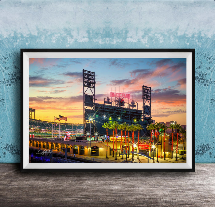 A framed photograph of a baseball stadium at sunset, with the stadium's lights and surrounding palm trees illuminated against a colorful sky.