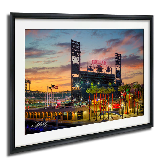 A framed photograph depicting a baseball stadium at sunset, with the stadium lights and surrounding palm trees illuminated against a colorful sky.