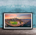 A framed aerial view of a baseball stadium and its surrounding cityscape at sunset.