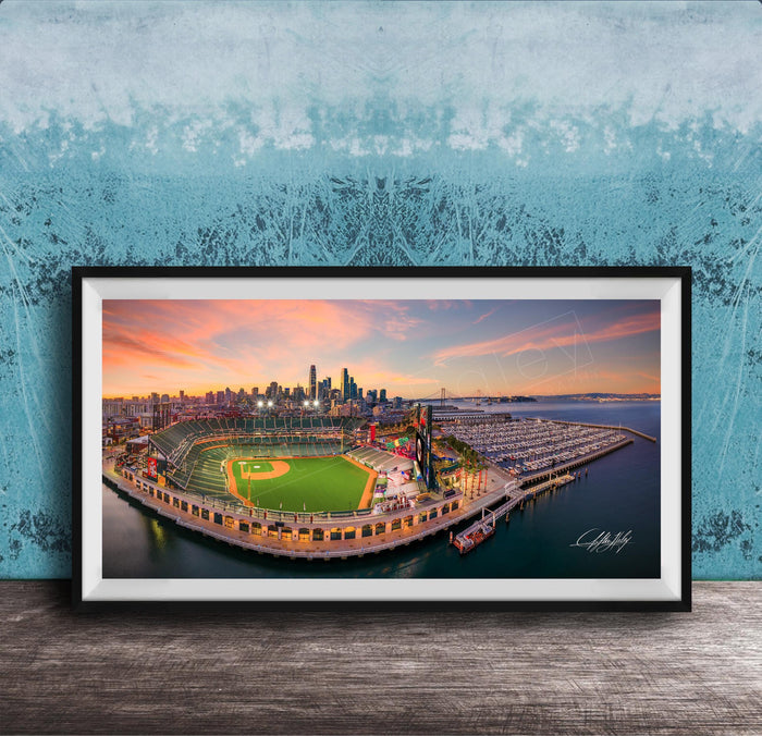 A framed aerial view of a baseball stadium and its surrounding cityscape at sunset.