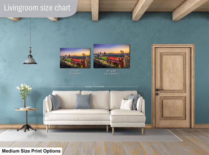 a living room with a white sofa and a wooden door. Above the sofa, there are two framed pictures hanging on the wall, depicting a cityscape at sunset. The living room has a blue wall and a wooden ceiling.