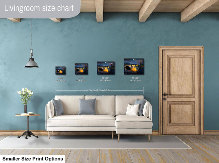 a living room with a white sofa, a wooden door, and a hanging light fixture. There are four framed artworks displayed on the wall, each with a different size and frame. The living room appears to be designed for relaxation and comfort, with a focus on the artwork and the overall aesthetic.