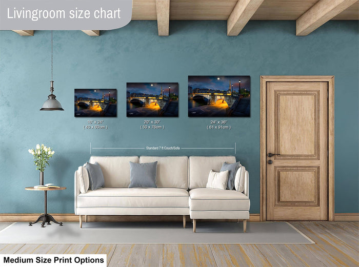 The image is a livingroom size chart with three framed prints of a nighttime cityscape, each with a different size ranging from 10x12" to 24x36" and 24x36" to 36x48". The prints are displayed above a white couch, and there is a wooden door and a small table with a vase of flowers in the room.