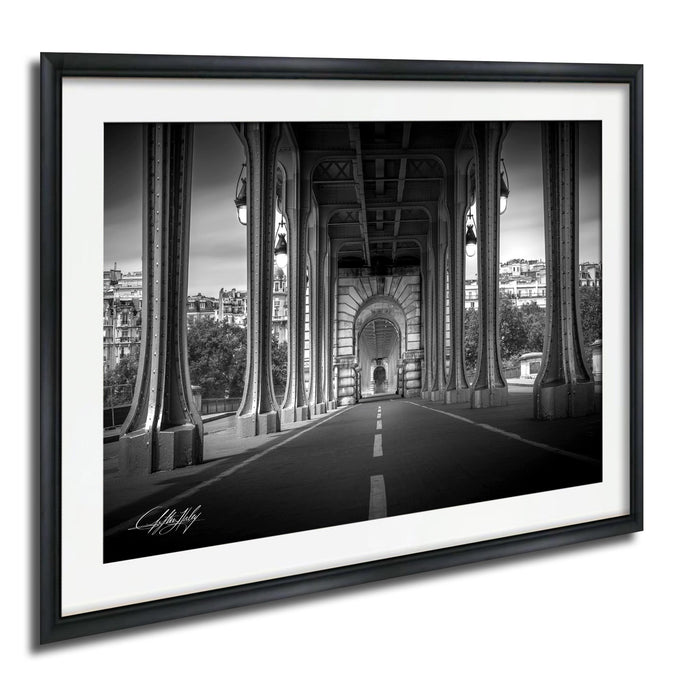 A black and white photograph of a bridge with tall columns and arches, leading to a road or walkway. The bridge appears to be an architectural landmark, with the surrounding buildings and trees visible in the background.