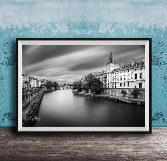 A black and white photograph of a cityscape with a river running through it, featuring a tall building with a clock tower in the background.