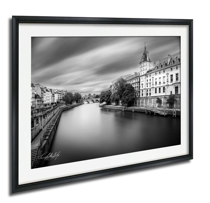 A black and white photograph of a cityscape with a river running through it, featuring a tall building with a clock tower in the background.