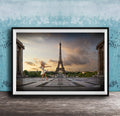 A framed photograph of a woman in a white dress dancing in front of the Eiffel Tower in Paris, France, with a blue sky and clouds in the background.