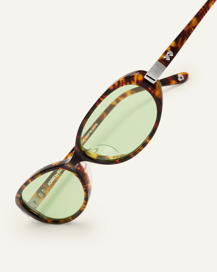 Close-up shot of Bonnie Clyde Pixie sunglasses in tortoise with green lenses.