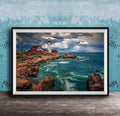 A framed photograph of a lighthouse on a rocky coastline, with the ocean and cloudy sky visible in the background.