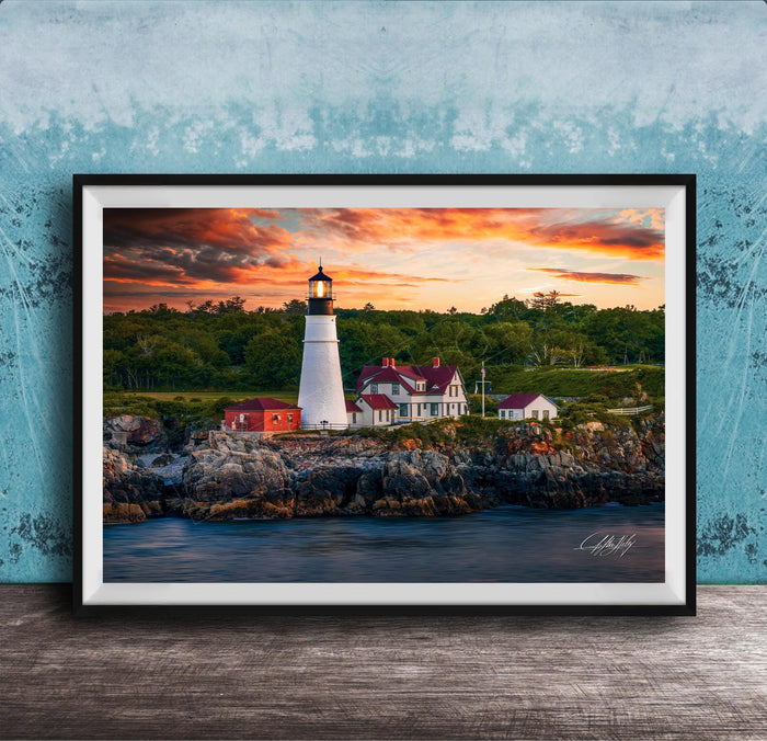 A framed photograph of a lighthouse on a rocky shore, with a colorful sunset sky in the background.