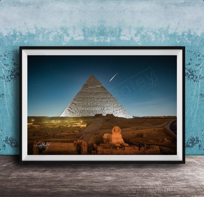 A framed photograph of the Great Pyramid of Giza at night, with the pyramid illuminated against a dark blue sky.