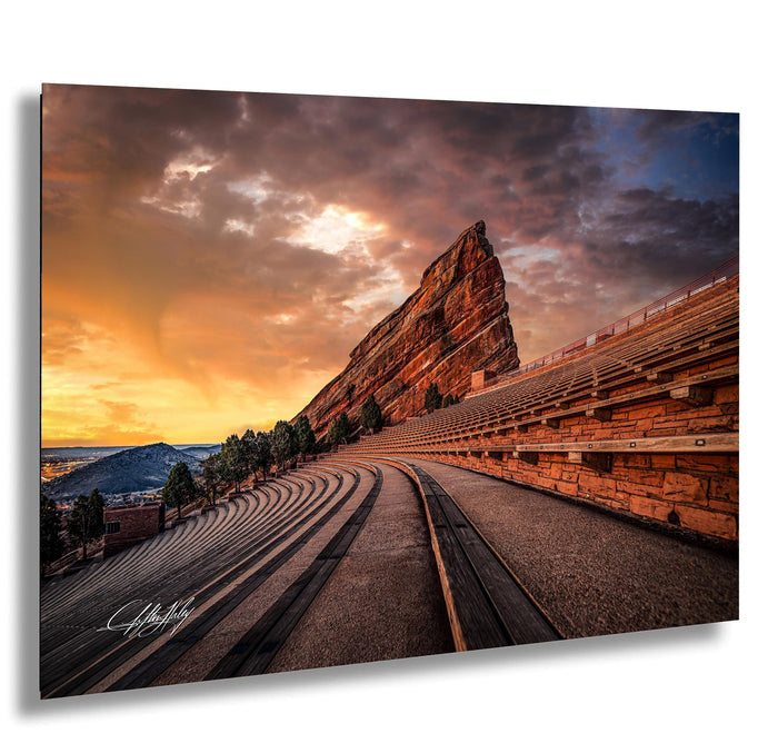 a large, steep rock formation with a winding path leading up to it, set against a dramatic sky with vibrant orange and purple hues.
