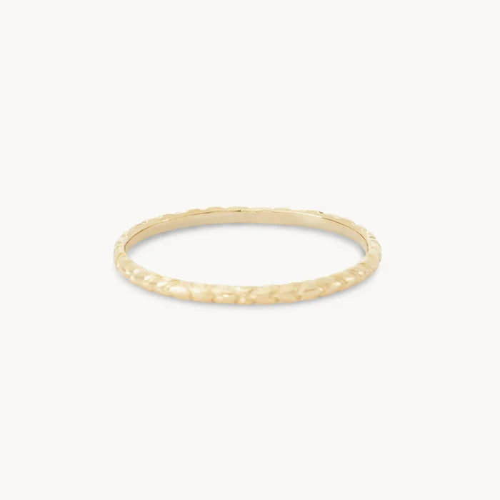A thin, textured gold ring against a plain white background. The revival stacking ring - 14k yellow gold by bluboho has a delicate, hammered finish that gives it a subtle, uneven surface.