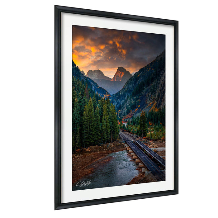 a scenic mountain landscape with a river, train tracks, and a dramatic sky with clouds and a sunset.