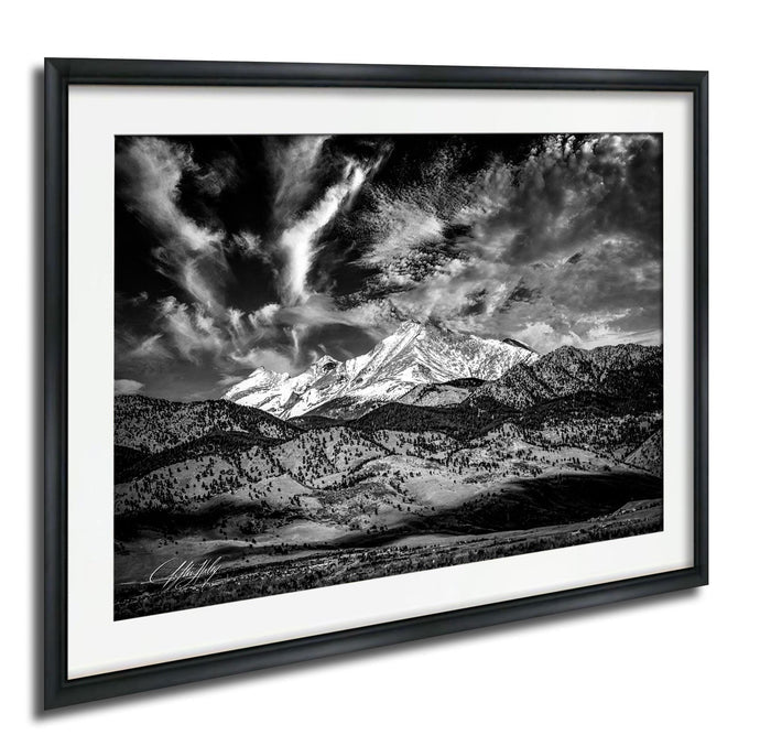 A dramatic black and white landscape photograph of a mountainous terrain, with a prominent snow-capped peak in the background and dramatic clouds in the sky.