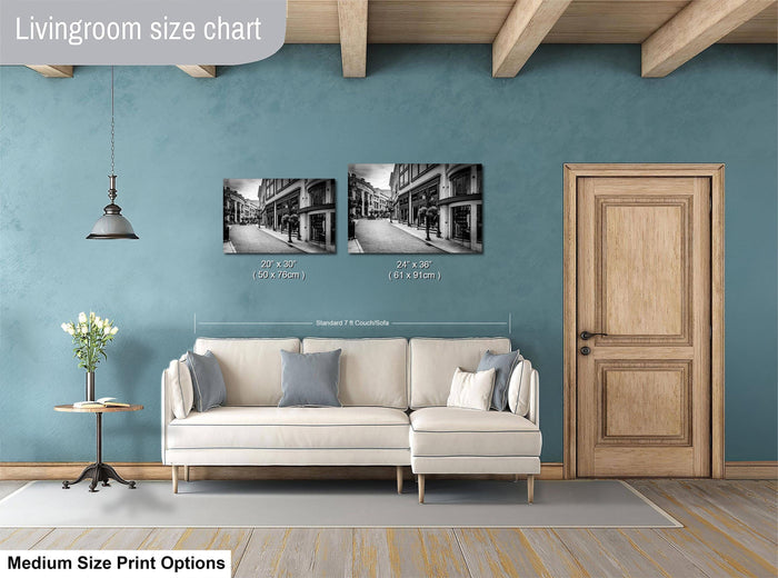 a living room with a white sofa, a wooden door, and a hanging light fixture. Above the sofa, there are two framed black and white photographs of a street scene. The wall behind the sofa has a blue color, and the floor is covered with a gray rug.