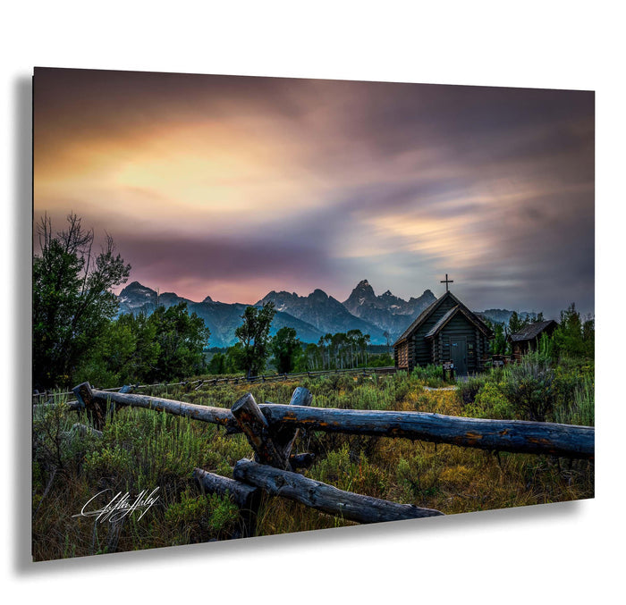 a serene rural landscape with a wooden fence, a small wooden building, and a mountain range in the background, all bathed in the warm glow of a colorful sunset.