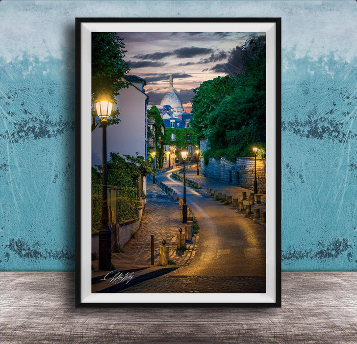 a picturesque street scene in Paris, France, with a cobblestone road lined with trees and lampposts, leading towards a large domed building at the end of the street.