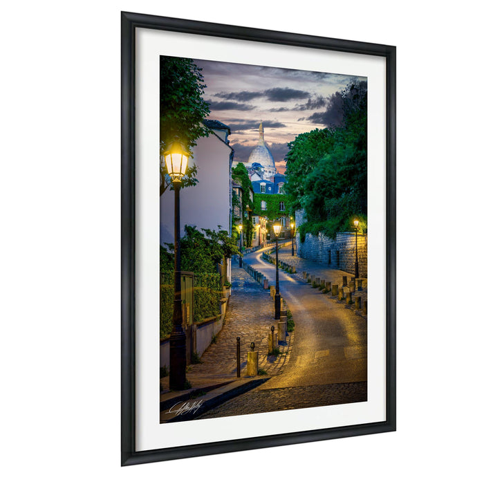 a picturesque street in Paris, France, with a domed building and a lamp post on the left side. The street is lined with trees and illuminated by street lamps, creating a warm and inviting atmosphere. The sky is filled with clouds, suggesting an overcast day. The overall scene is serene and charming, capturing the essence of a typical Parisian evening.