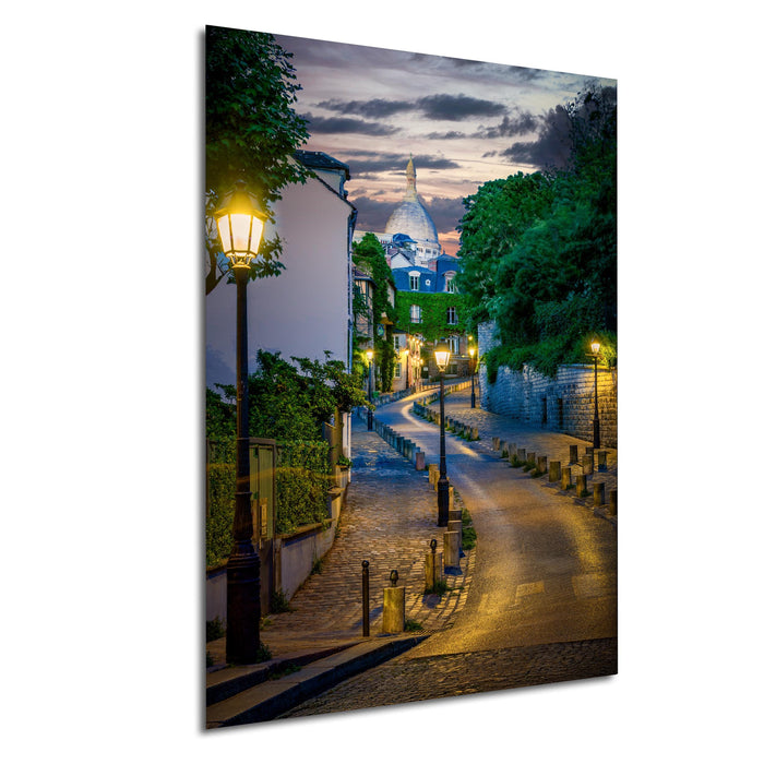 a picturesque street in Paris, France, with a domed building in the background and a lamp post on the left side. The street is lined with trees and illuminated by street lamps, creating a warm and inviting atmosphere.