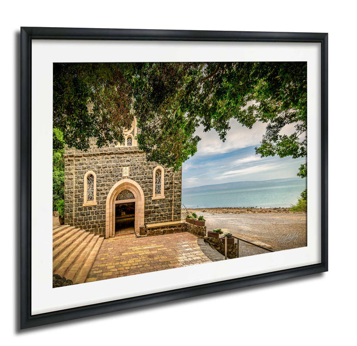 A stone church with a brick walkway and a stone wall, surrounded by trees and overlooking a body of water.