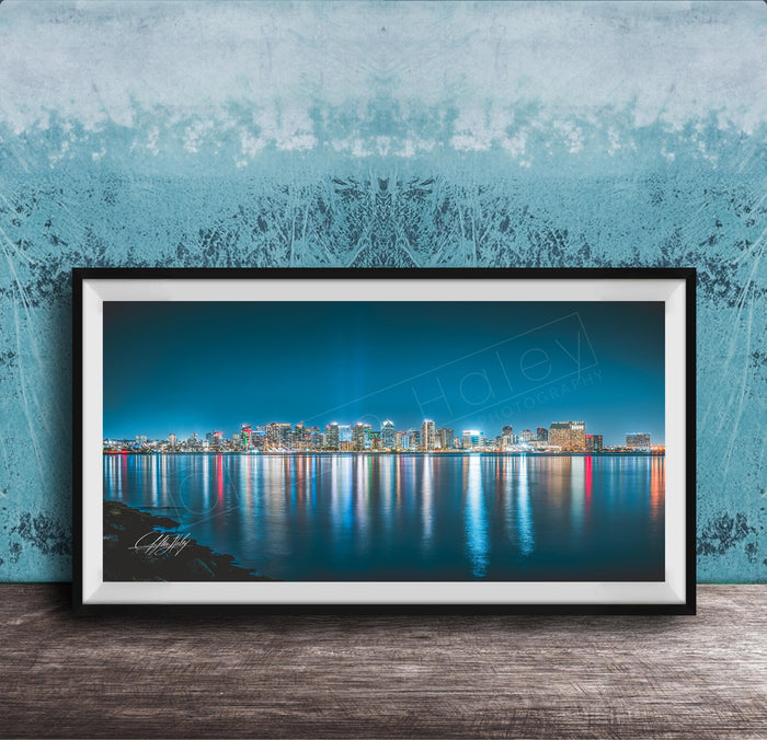 A framed photograph of a city skyline at night, with the buildings' lights reflected in the water below.