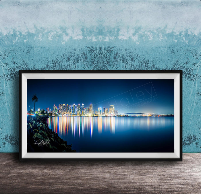 A framed photograph of a city skyline at night, with the city's lights reflected in the water below.