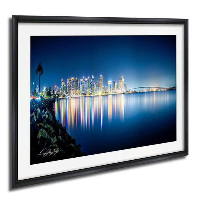 A framed photograph depicting a city skyline at night, with the city lights reflected in the water below.